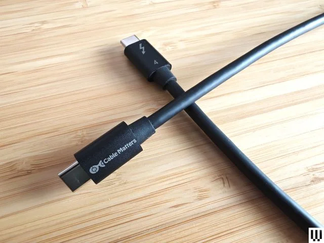 Top view of Cable Matters USB-C to USB-C Thunderbolt 4, 2 black cords crossing over each other while on a wooden surface