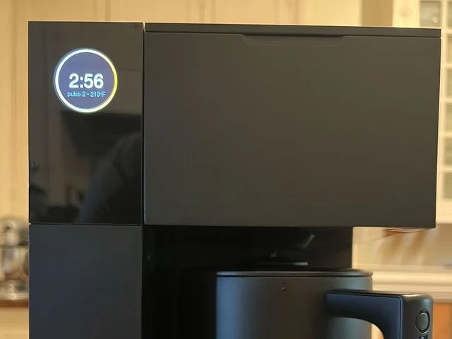 Front view of the Fellow Aiden Precision Coffee Maker, a black, rectangular coffee maker with small digital screen on the left and a large black coffee pot