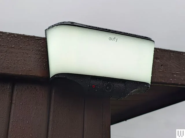 Rectangular security camera with white panel attached to corner of a roof