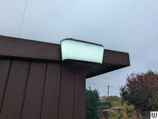 Rectangular security camera with white panel attached to corner of a roof