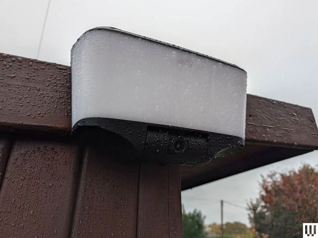 Rectangular security camera with white panel attached to corner of a roof
