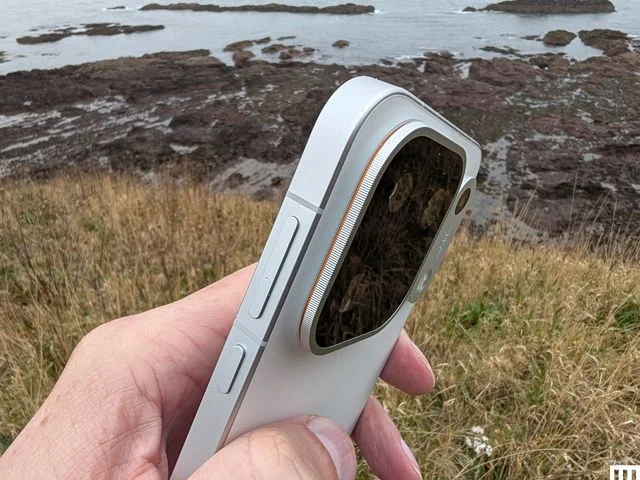 Closeup of side of a white slim mobile phone a rocky coastline in the distance