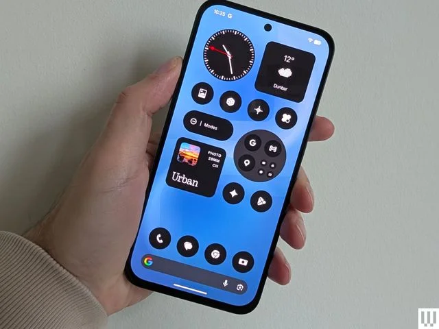 A slim mobile phone in a person's hand with the screen showing widgets like time weather and music app