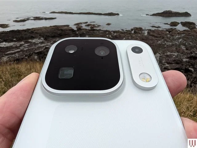 Closeup of the rear camera lenses on a slim mobile phone a rocky coastline in the distance
