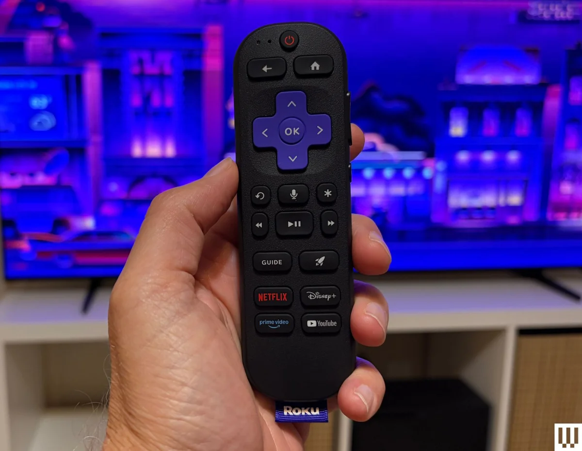 Hand holding small black tv remote with rounded edges and rounded buttons