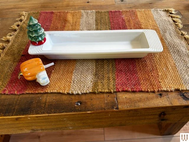 White ceramic tray with decorative mini tree on the left ledge and mini pumpkin on the table