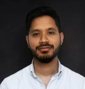 A Bivu Das wearing a light blue collared shirt stands against a dark background, showcasing a neutral expression.